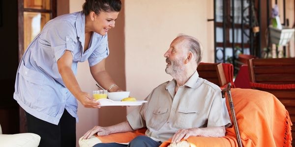 Caregiver serving meal to elderly man at home